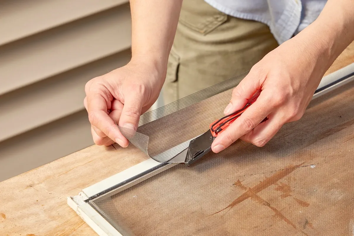 Woman cuts excess screen after replacing window screen and spline.