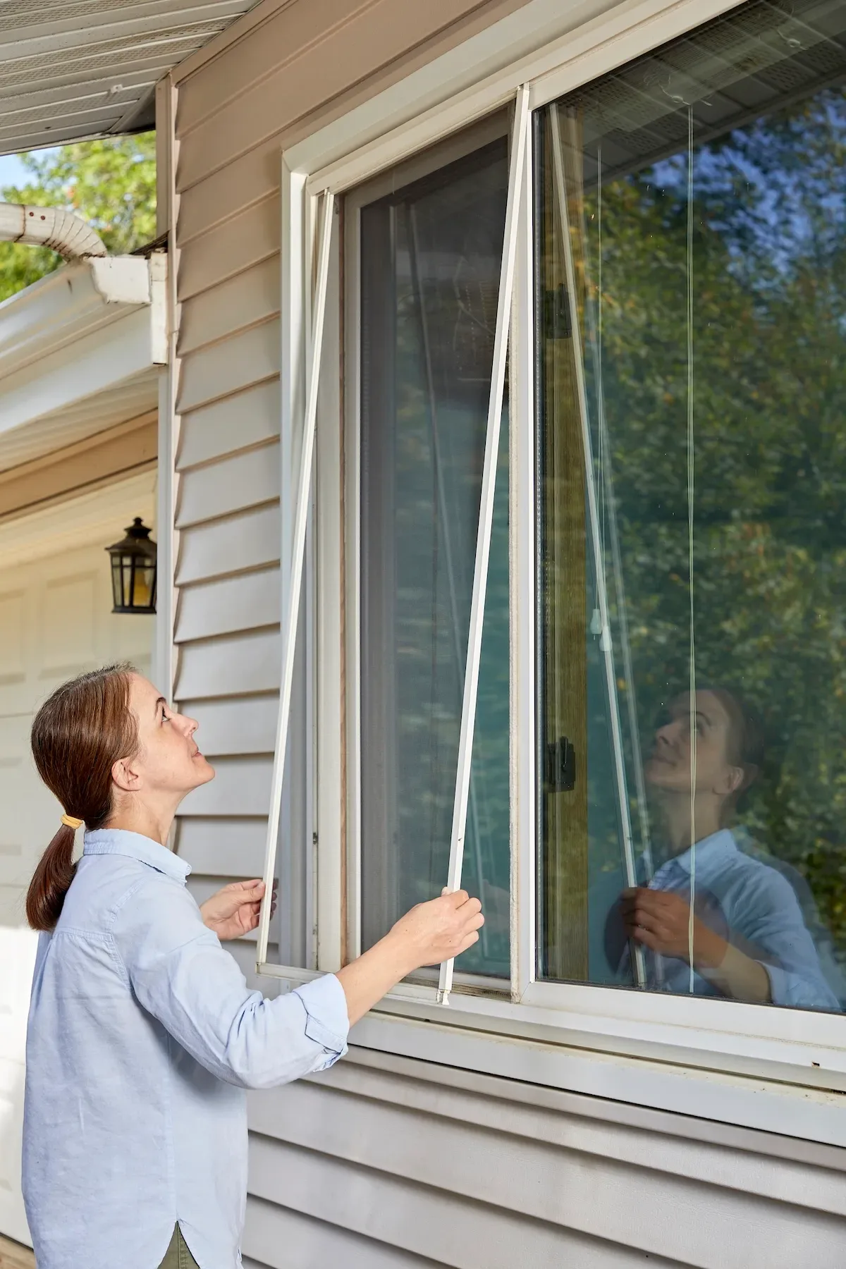 Woman replaces new window screen in window frame.