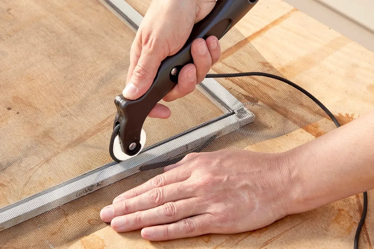 Woman uses a spline wheel to push spline into window screen channel.